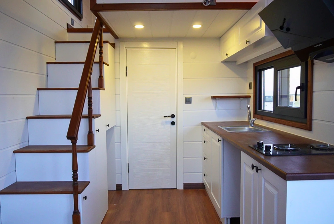 Tiny House iç tasarımı – beyaz mutfak dolapları, ahşap merdiven ve loft alanlı minimalist yaşam alanı